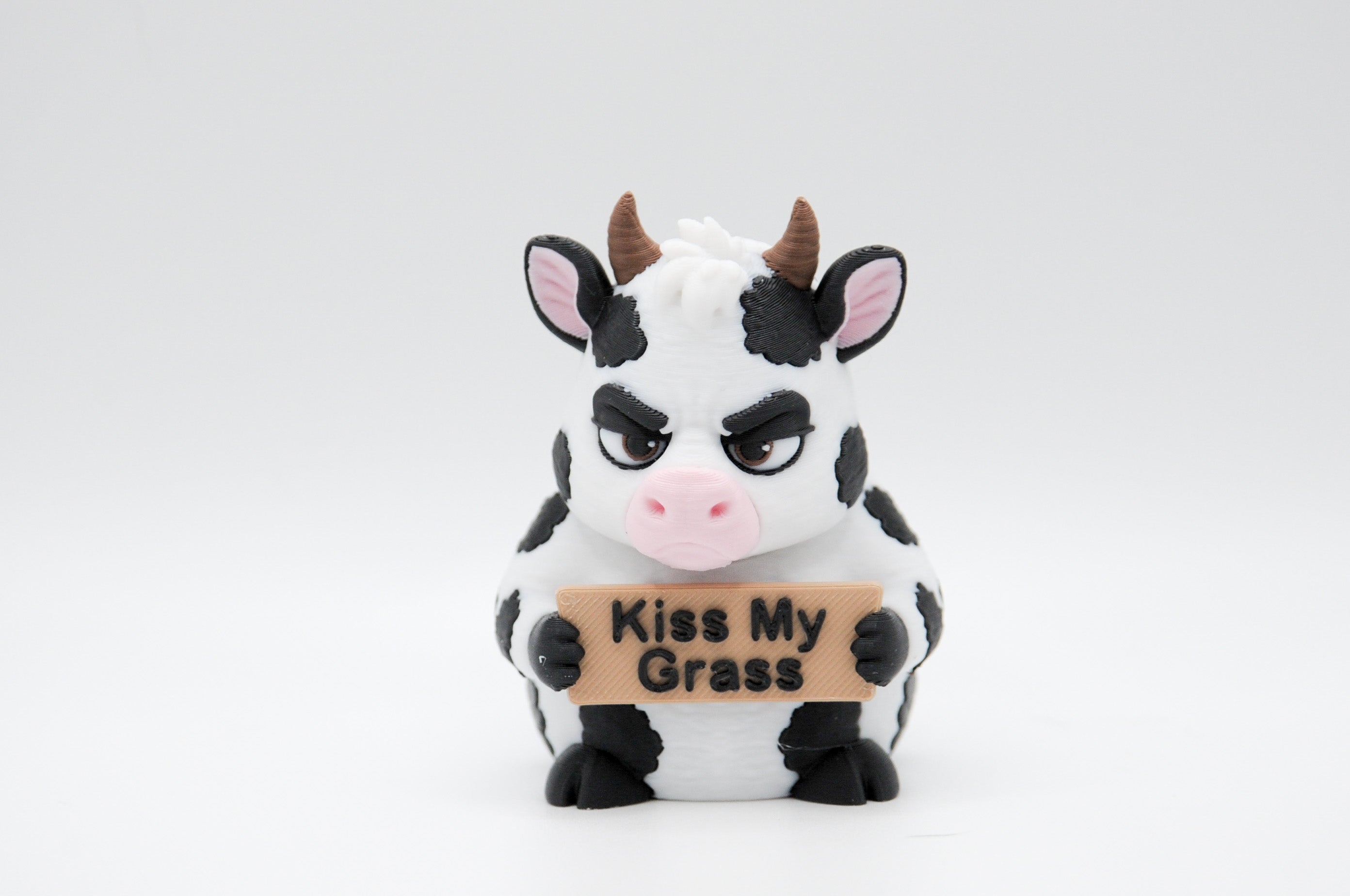 Cow holding a Kiss My Grass sign