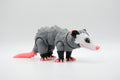 Gray opossum figure with white face and bright pink tail