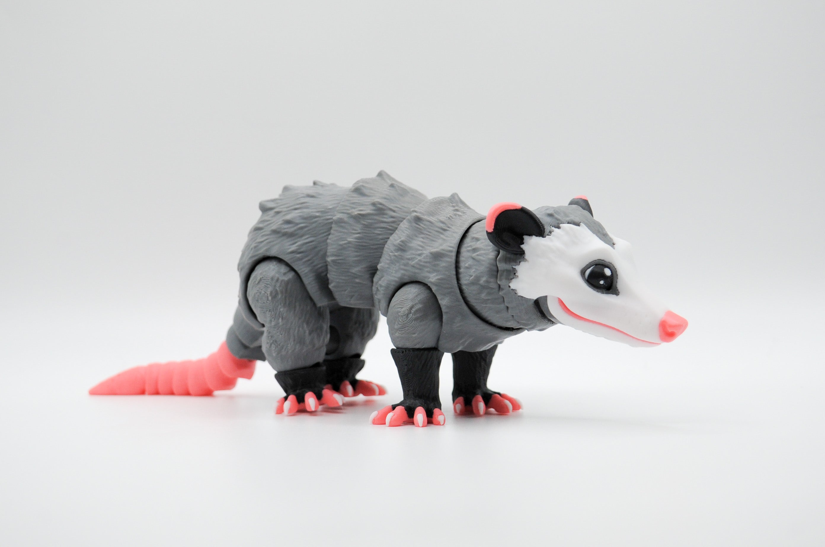 Gray opossum figure with white face and bright pink tail