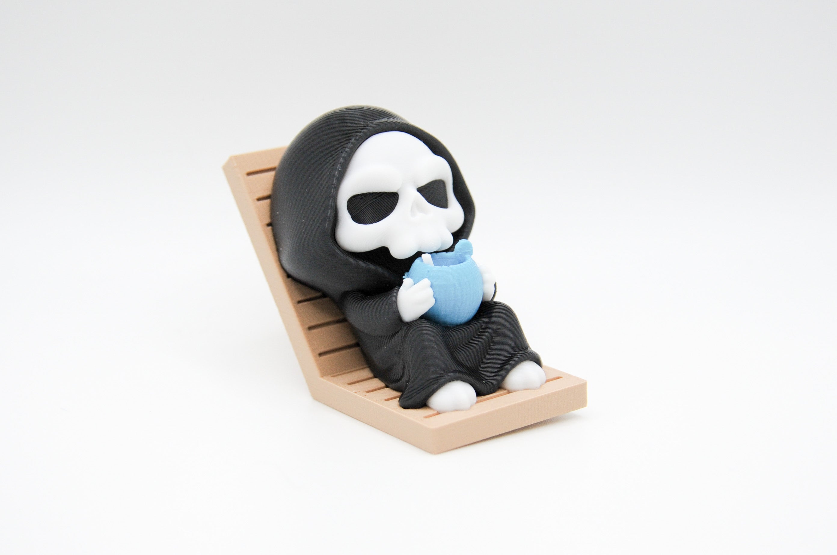 Hooded reaper figure reclining in a lounge chair with a blue drink